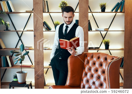 Handsome young man in elegant suit reading a book in modern luxury interior Handsome young man in elegant suit reading a book in modern luxury interior 59246072