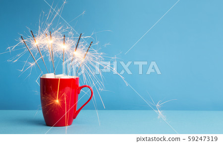 Cocoa and marshmallow in Red cup with sparklers on blue Cocoa and marshmallow in Red cup with sparklers on blue 59247319
