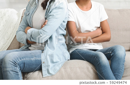 Two sisters with arms crossed sitting next to each other 59249474