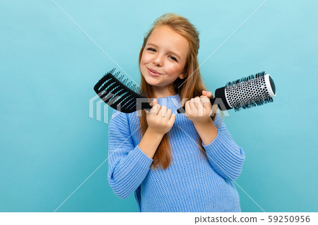schoolgirl model on a blue background posing with a comb in her hands 59250956