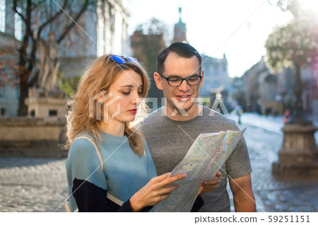Tourists couple looking at the paper map and searching for direction early in the morning on empty Tourists couple looking at the paper map and searching for direction early in the morning on empty 59251151