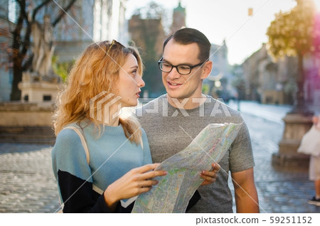 Happy young couple holding a touristic map of ancient European city early in the morning on empty Happy young couple holding a touristic map of ancient European city early in the morning on empty 59251152