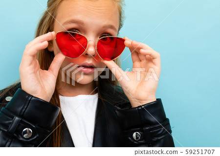 Close-up portrait of a stylish schoolgirl on a blue background with red sunglasses 59251707
