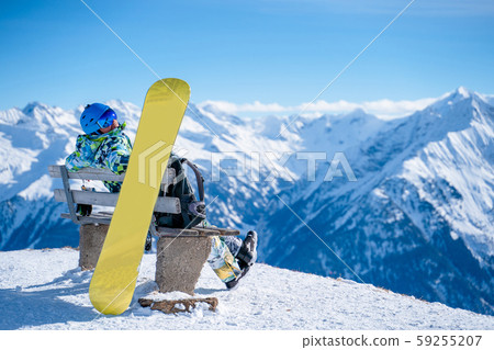 Image from back of athlete man sitting on bench next to snowboard in ski resort. Image from back of athlete man sitting on bench next to snowboard in ski resort. 59255207