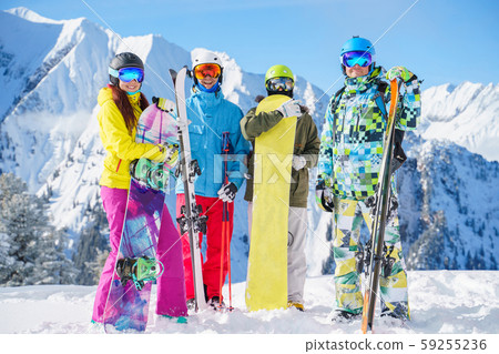 Photo of two sports women and two men with skis and snowboard standing at ski resort 59255236