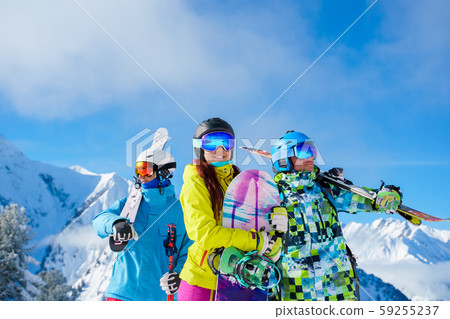 Two men and woman with snowboard and skis looking in different directions standing on snow resort Two men and woman with snowboard and skis looking in different directions standing on snow resort 59255237