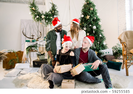 Group of happy multiracial friends laughing and sharing Christmas gifts in beautiful cozy studio 59255585