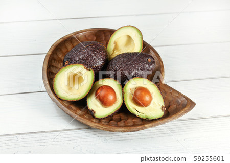Ripe dark brown avocados - Hass Bilse variety - some cut in half, seeds visible, in wooden carved 59255601