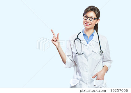 Friendly smiling young female doctor. hand pointing at copy space. isolated on a light blue Friendly smiling young female doctor. hand pointing at copy space. isolated on a light blue 59257006