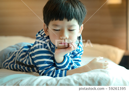 Portrait of a cute little asian boy lying down alone on the bed feeling sad or upset. Child development, Unwell, Sickness, Emotional, Wednesday's Child, Left alone, Neglected, Child development. 59261395