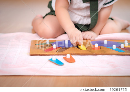 Closeup: Hands of a preschool little girl 2-3 years in Montessori classroom engaged sensory wooden puzzle activity. 10 fingers, Fine motor skills, Montessori method, Tools, Child development concept. Closeup: Hands of a preschool little girl 2-3 years in Montessori classroom engaged sensory wooden puzzle activity. 10 fingers, Fine motor skills, Montessori method, Tools, Child development concept. 59261755
