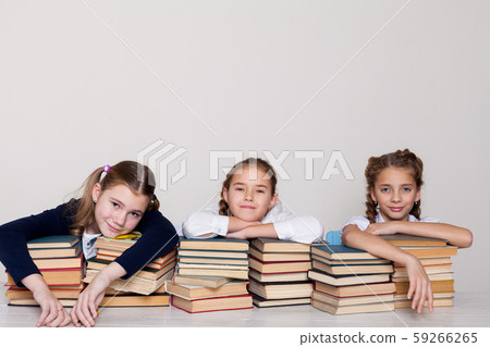three schoolgirl girls with books in the library in class at the desk 59266265