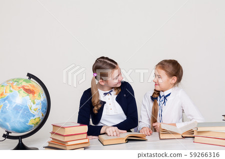 two schoolgirl girls with books and a globe in class at the desk two schoolgirl girls with books and a globe in class at the desk 59266316