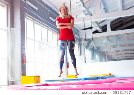 Fitness, fun, leisure and sport activity concept - Young happy woman jumping on a trampoline indoors Fitness, fun, leisure and sport activity concept - Young happy woman jumping on a trampoline indoors 59281797