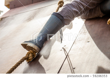 Young boy in wellys climbing up a wall with ropes 59286353