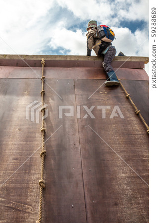 Young boy in wellys climbing up a wall with ropes Young boy in wellys climbing up a wall with ropes 59288689