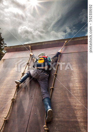 Young boy in wellys climbing up a wall with ropes Young boy in wellys climbing up a wall with ropes 59288692