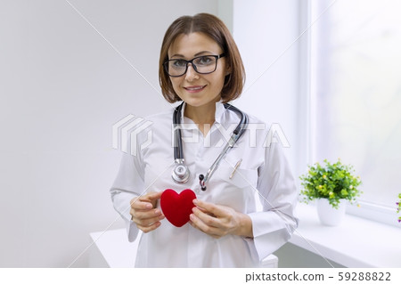 Female doctor with stethoscope holding heart, background hospital window Female doctor with stethoscope holding heart, background hospital window 59288822