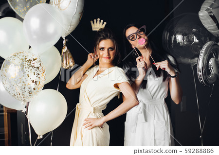Two young ladies holding accessories and posing at 59288886