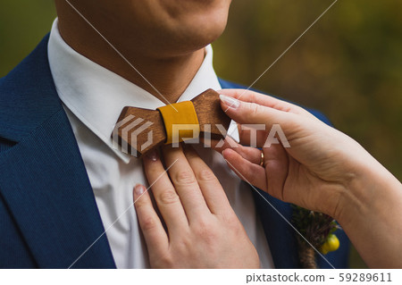 Caring bride straightening wooden bow tie to groom 59289611