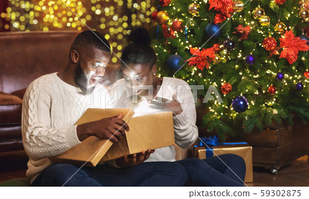 Dazed black couple opening xmas gift box in living room near Christmas tree 59302875