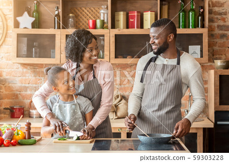 Mother teaching daughter cutting vegetables, father frying food 59303228