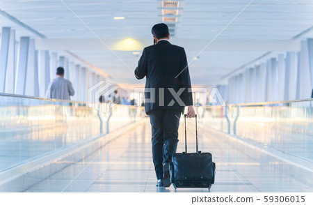 Businessman walking and wheeling a trolley suitcase at the lobby, talking on a mobile phone Businessman walking and wheeling a trolley suitcase at the lobby, talking on a mobile phone 59306015