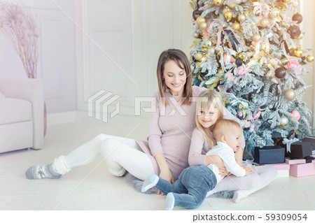 Portrait of cute adorable little blond children with mother enjoy sitting near christmas tree in 59309054
