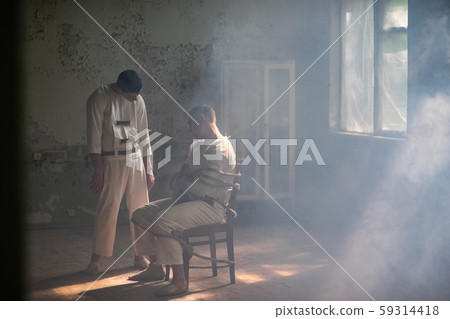 A crazy man in a straitjacket is tied to a chair in an abandoned old clinic and the other insane man 59314418