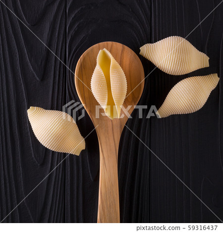 Top view of conchiglie pasta shells on black wooden table with spoon 59316437