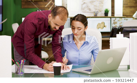 Female chief architect taking a sip of coffee and helping her colleague 59321447