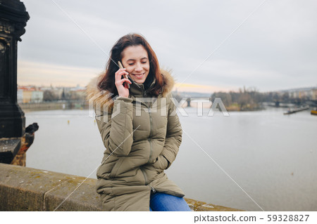 Smiling tourist woman in Prague speaking on smartphone. Young woman tourist stands on the Charles 59328827