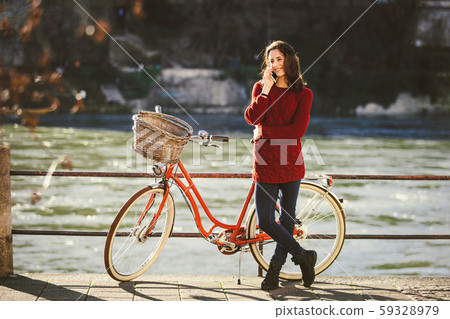 A young female traveler enjoying stands next to a bicycle near a river in the city of Basel 59328979