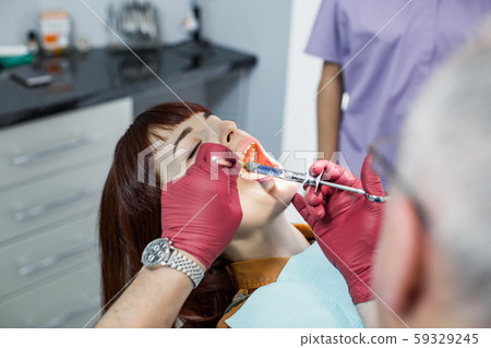 Young pretty woman at the dentist. Injection with anesthesia performed by a senior man doctor and Young pretty woman at the dentist. Injection with anesthesia performed by a senior man doctor and 59329245