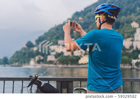 Cyclist taking pictures with smart phone. Caucasian man in bike helmet taking photo of landscape Cyclist taking pictures with smart phone. Caucasian man in bike helmet taking photo of landscape 59329582