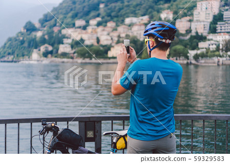 Cyclist taking pictures with smart phone. Caucasian man in bike helmet taking photo of landscape Cyclist taking pictures with smart phone. Caucasian man in bike helmet taking photo of landscape 59329583