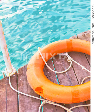 Orange lifebuoy with rope on a wooden pier near sea. 59333549