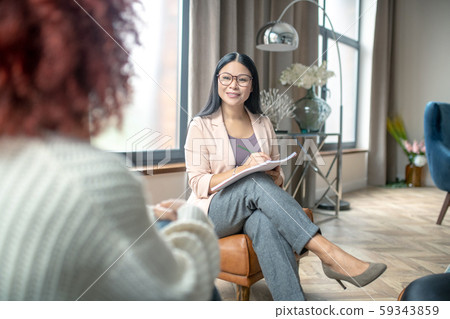 Pleasant psychologist wearing grey trousers smiling to client Pleasant psychologist wearing grey trousers smiling to client 59343859