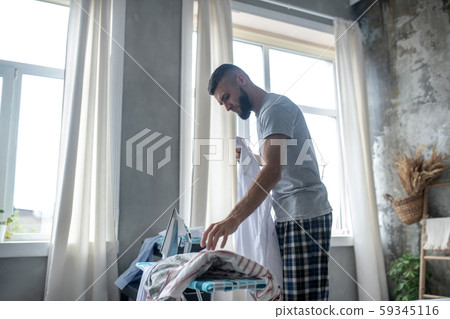 Bearded man standing near window and ironing Bearded man standing near window and ironing 59345116