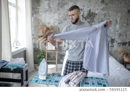 Dark-haired businessman doing ironing at the weekend Dark-haired businessman doing ironing at the weekend 59345125