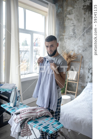 Serious dark-haired man ironing shirt in the bedroom 59345135