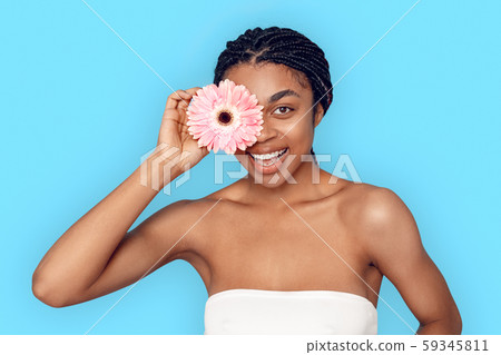 Beauty Concept. Young african woman isolated on blue covering eye with flower smiling playful Beauty Concept. Young african woman isolated on blue covering eye with flower smiling playful 59345811