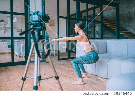 Slim fitness blogger doing sit ups while filming morning tutorial Slim fitness blogger doing sit ups while filming morning tutorial 59346440
