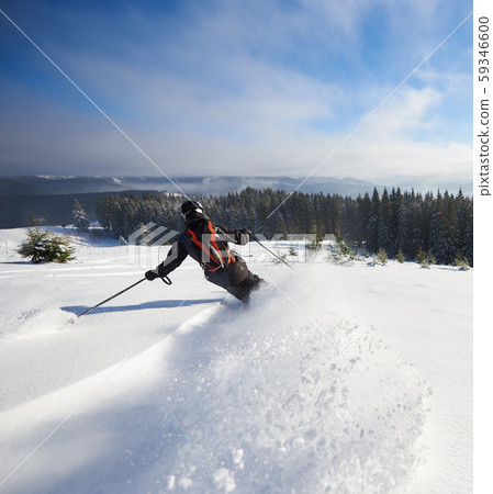 Male skier freeriding on wide open mountain slope. Extremal skiing down between low fir trees Male skier freeriding on wide open mountain slope. Extremal skiing down between low fir trees 59346600