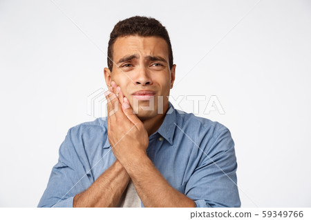 Medicine, people and emotions concept. Upset gloomy young man have discomfort, touch cheek and 59349766