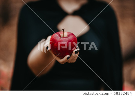 Woman as witch in black offers red apple as symbol of temptation, poison. 59352494