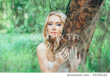 Portrait of young blond bride in forest holding tree 59356182