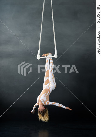 A young girl performs the acrobatic elements in the air trapeze. Studio shooting performances on a A young girl performs the acrobatic elements in the air trapeze. Studio shooting performances on a 59356493