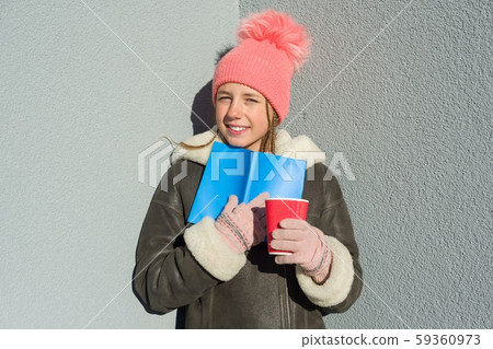 Winter outdoor portrait of young female student with book and cup Winter outdoor portrait of young female student with book and cup 59360973