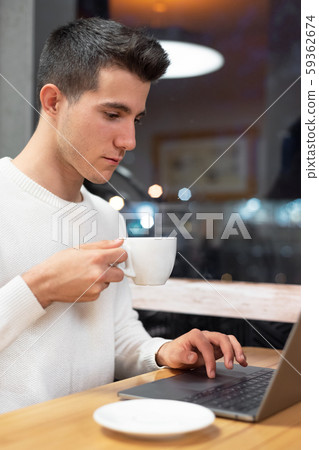 Young man working on his laptop in a coffee shop, young student typing on computer.  59362674